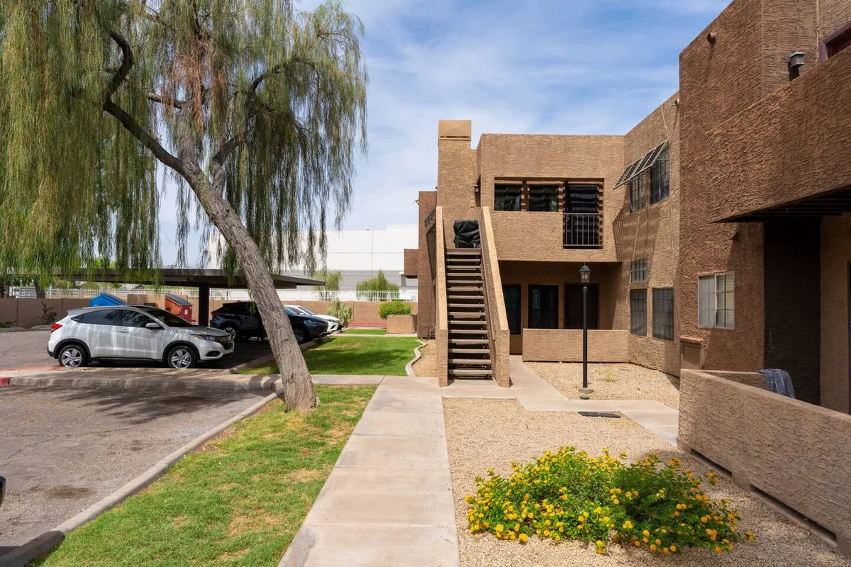 A relaxed exterior view with a staircase, lush greenery, vibrant flower bed, and a convenient parking area. The setting is welcoming and evokes a sense of community and accessibility, hinting at easy comings-and-goings for urban excursions.