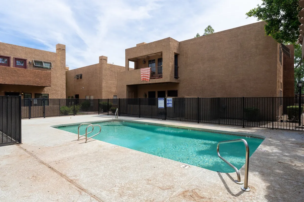 An inviting exterior view of the resort-style swimming pool, with the building facade and a flag hanging from a balcony. The atmosphere is relaxed, hinting at sunny days spent swimming or lounging poolside.