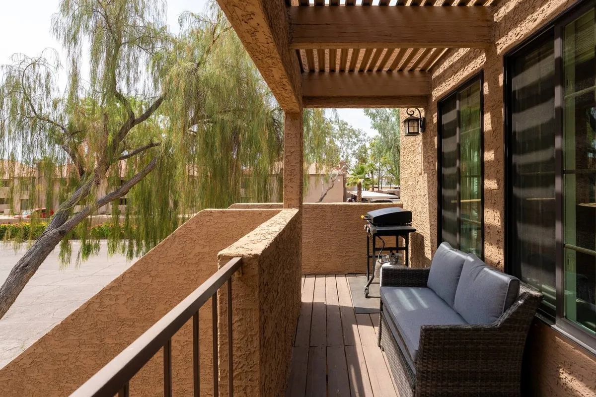 An inviting outdoor patio with a barbecue grill, comfortable seating, and lush greenery. The seating area is designed for casual relaxation or entertaining, with a view of the sunset possible from the balcony.