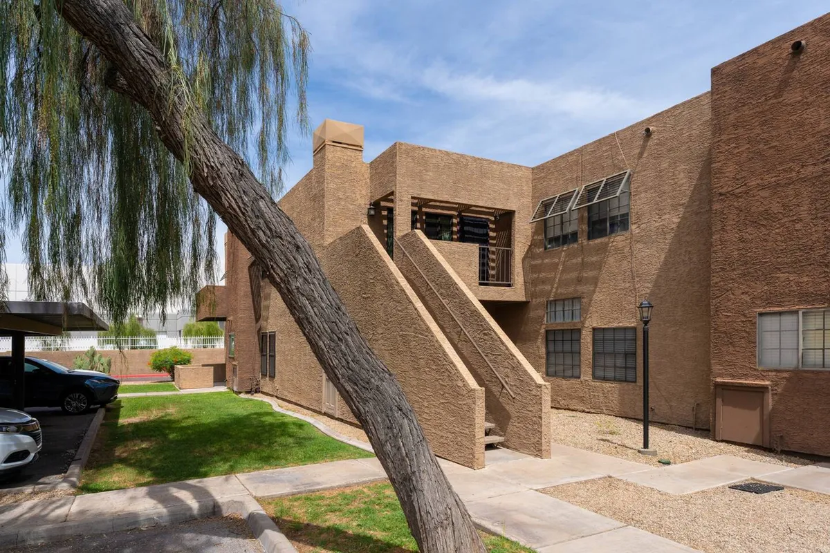 This exterior view features a staircase leading to the upper level of the condo, a leafy tree providing shade, and a visible parking area. The inviting scene hints at both the ease of access and outdoor relaxation possibilities.