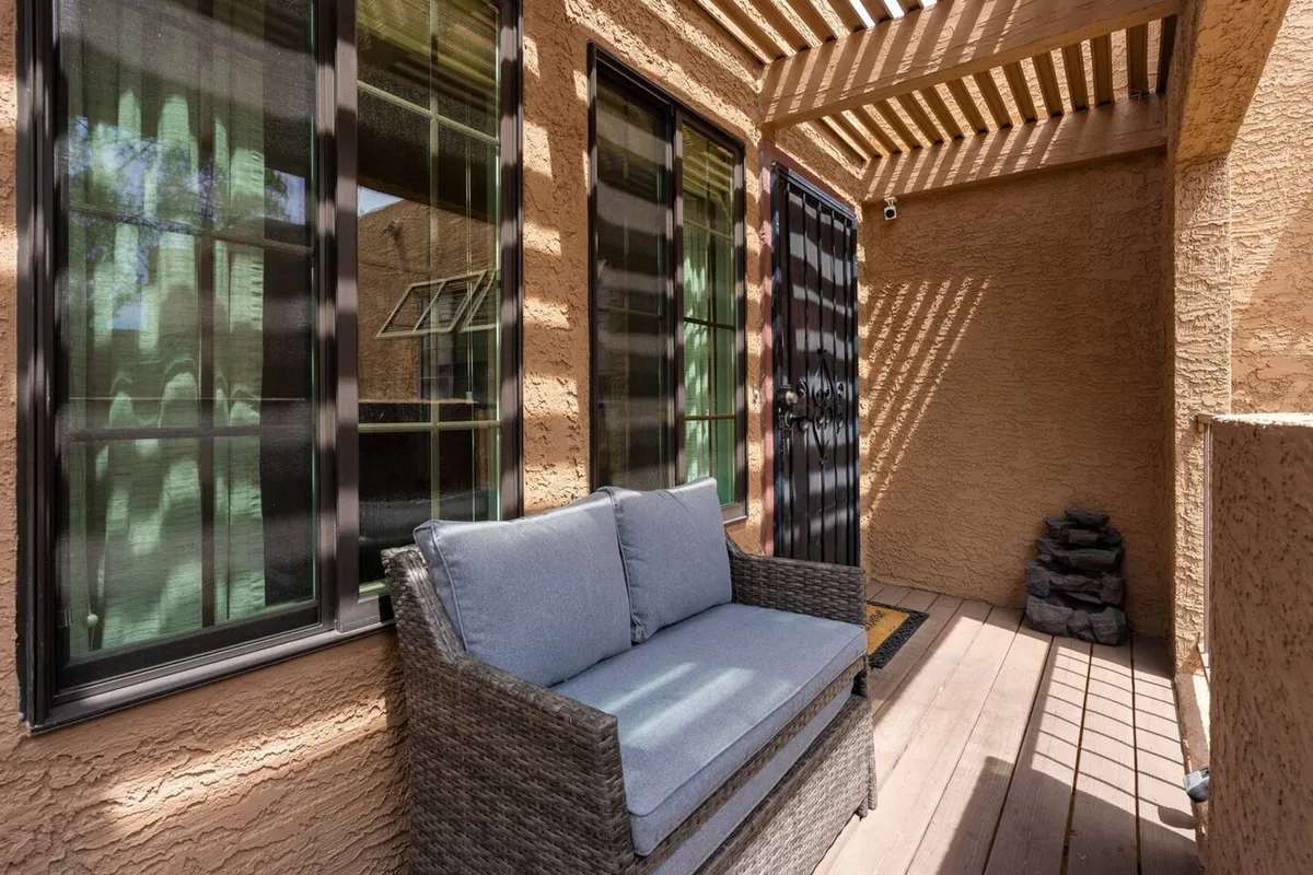 An inviting outdoor patio setup under a pergola, with a wicker sofa and decorative stones. The calm, shaded area suggests a comfortable place to relax or catch up on work outside.