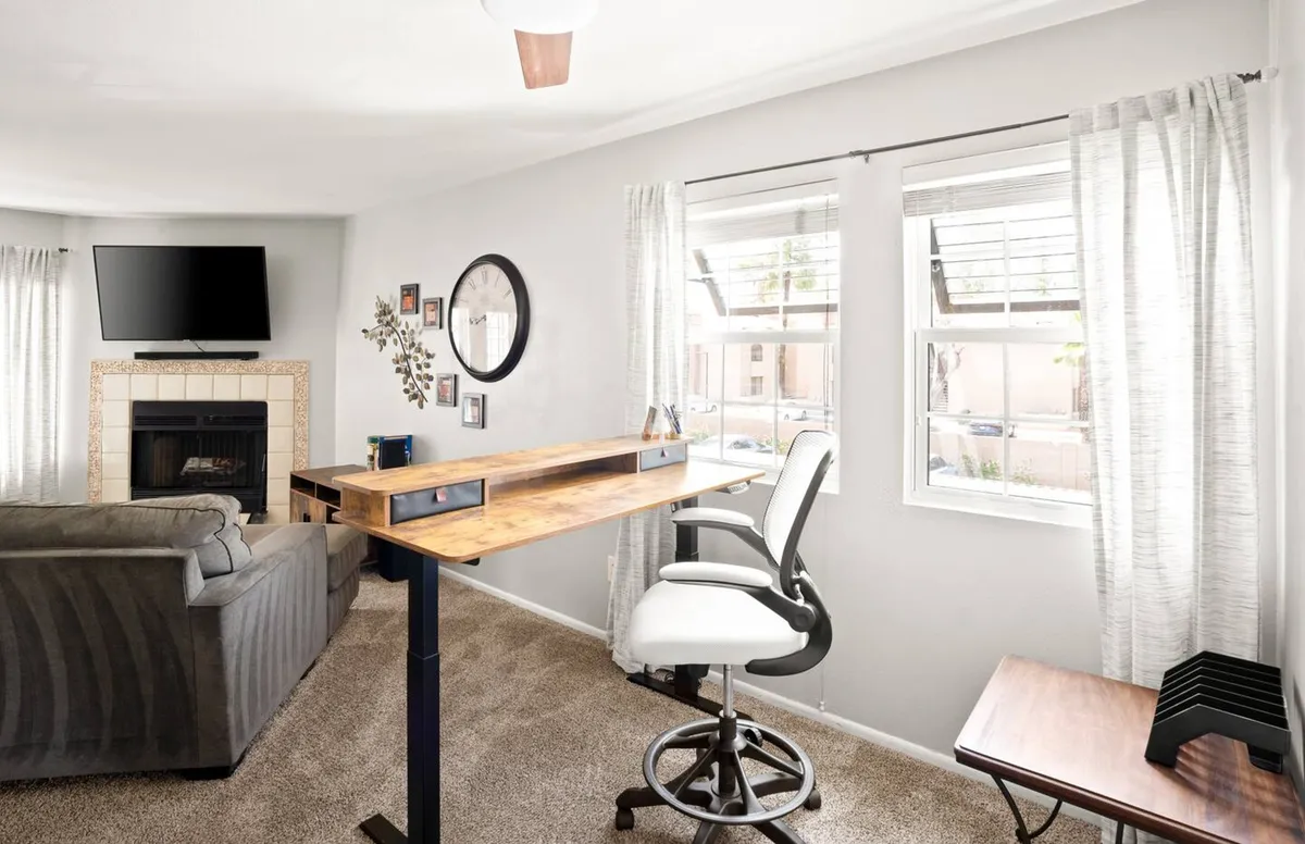 This image highlights a thoughtfully designed workspace featuring a standing desk near a window that floods the area with natural light. The scene also includes a cozy fireplace, a comfortable sofa, and curtains framing the window, creating a balanced environment for both productivity and relaxation.